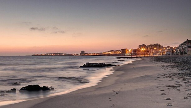Une plage avec une vue sur la ville en arrière-plan, au coucher du soleil.