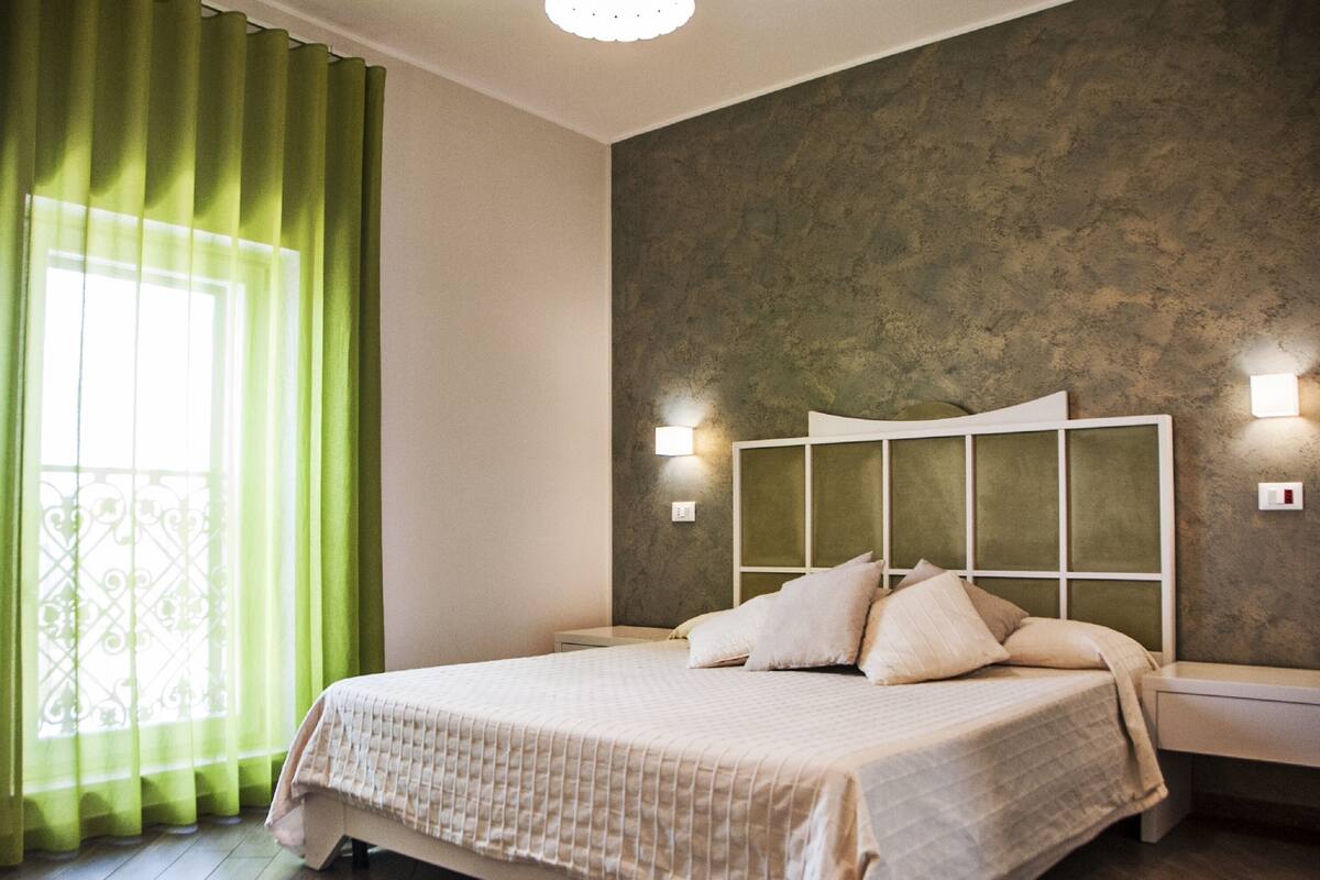 Una camera da letto con un letto, tende verdi, un muro strutturato e lampade da comodino.