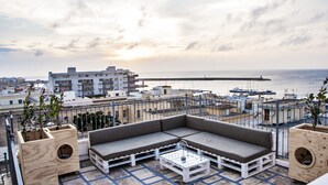 Une terrasse sur le toit, aménagée avec un canapé et une table basse, offrant une vue sur un port de plaisance et le paysage urbain.
