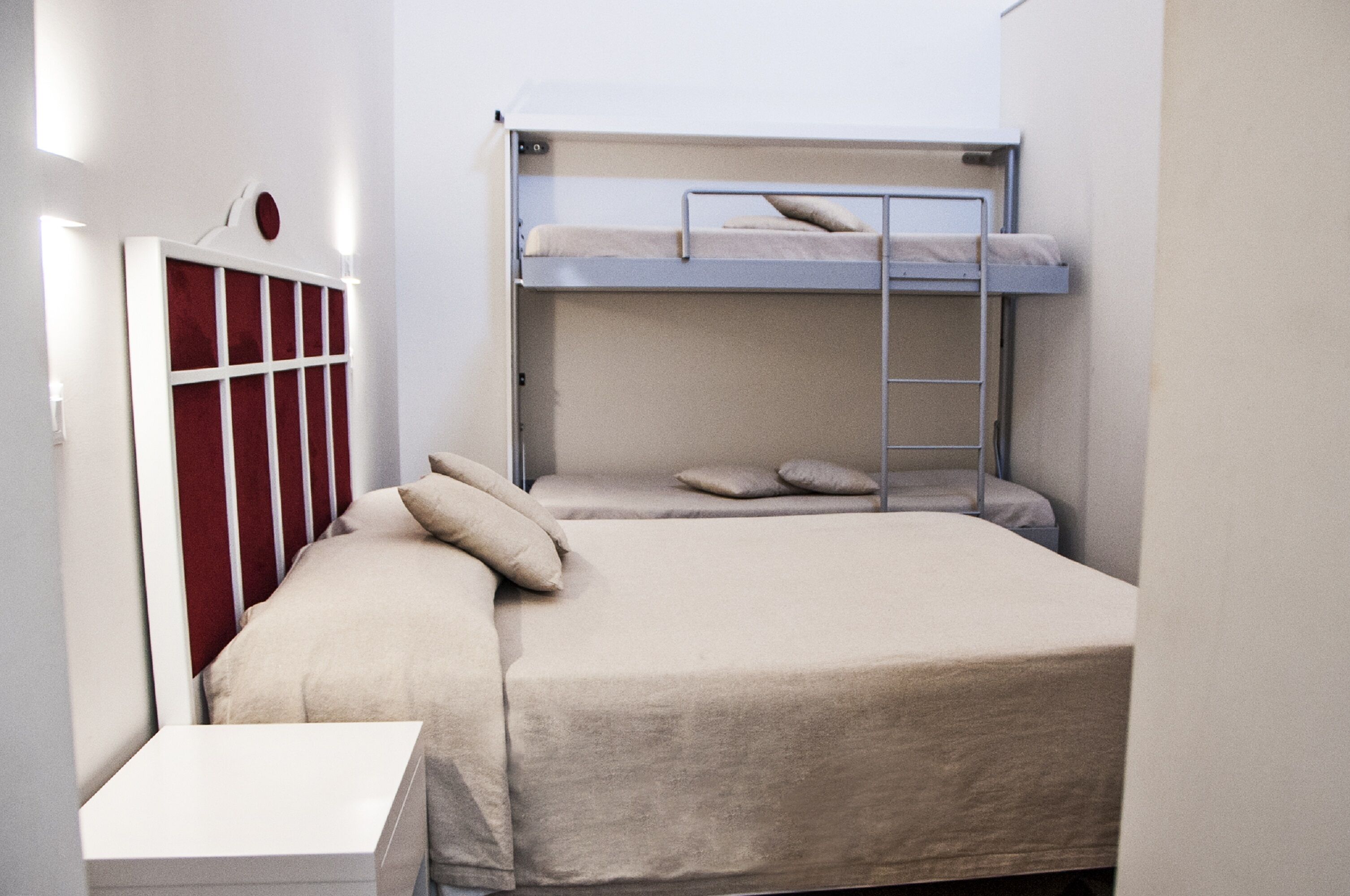 Habitación con literas, una cama individual y una litera superior. Incluye una mesita pequeña y un armario con espejo.