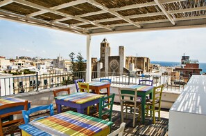 A rooftop terrace with colorful tables and chairs, overlooking a cityscape with historic buildings and a view of the sea. - B&B Ghalà (Gallipoli)