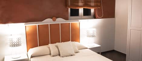 A neatly made bed with a headboard, two bedside tables with lamps, and a window with blinds.