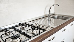 Une cuisine équipée d’une cuisinière à gaz, d’un évier en acier inoxydable et de meubles blancs.