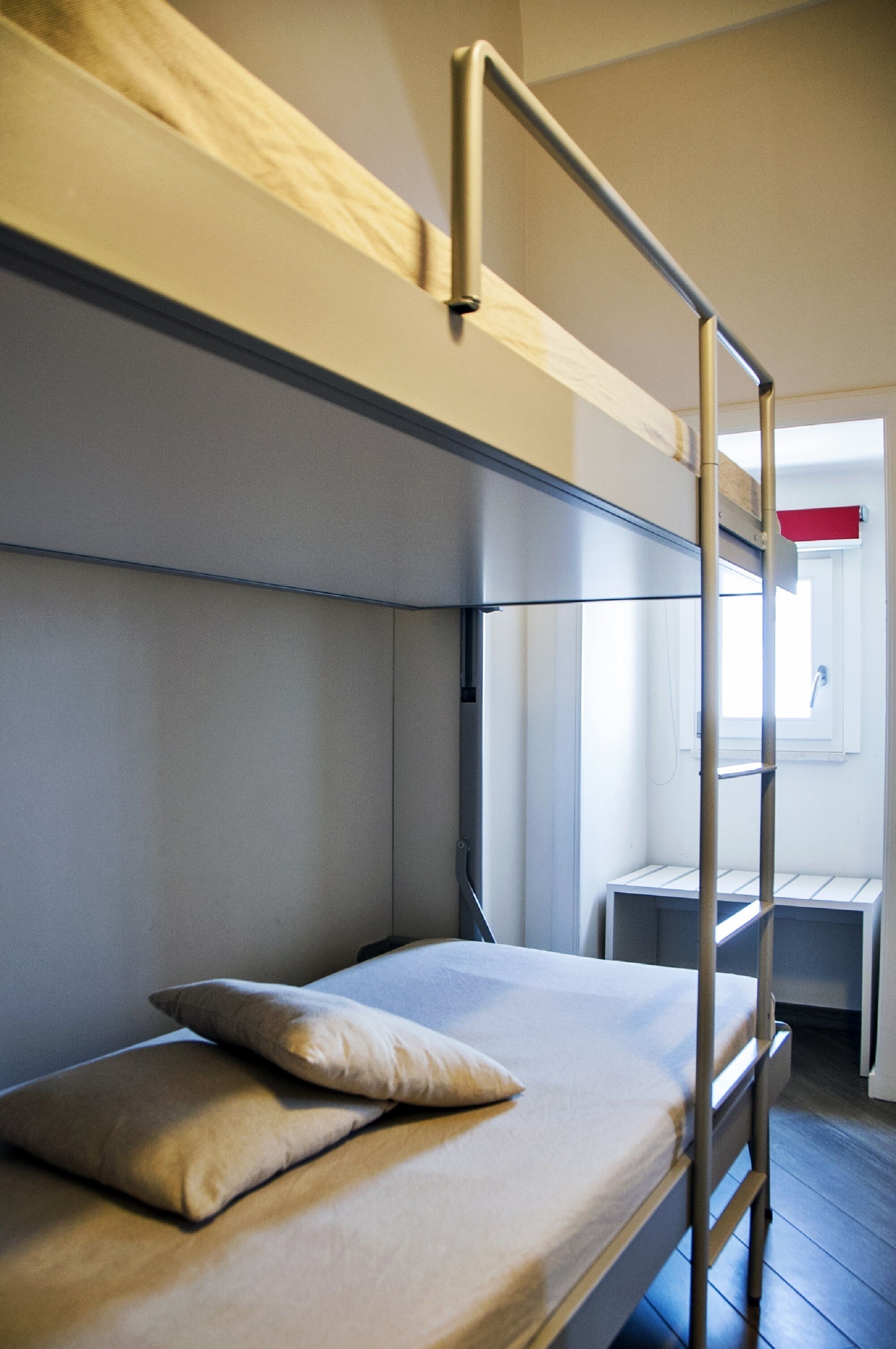 Un lit superposé avec une échelle, un seul oreiller et un petit bureau avec une chaise.