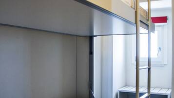 Un lit superposé avec une échelle, un seul oreiller et un petit bureau avec une chaise.