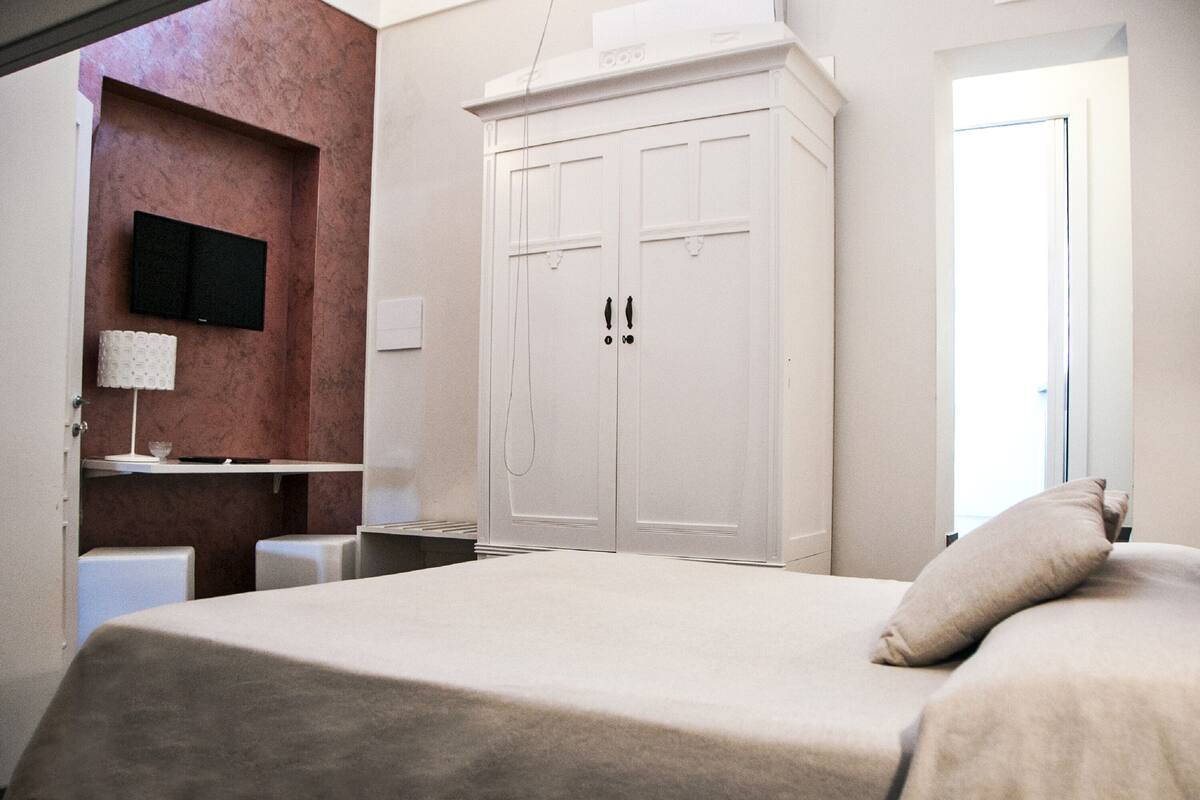 Una camera da letto con un letto, un armadio, una televisione a parete e un comodino con una lampada.