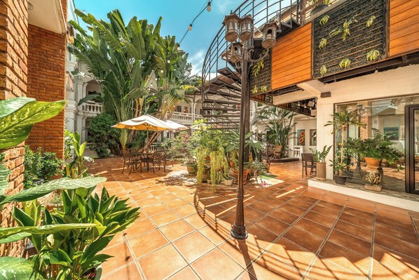 Un patio con suelo de baldosas, mobiliario exterior y diferentes macetas con plantas.