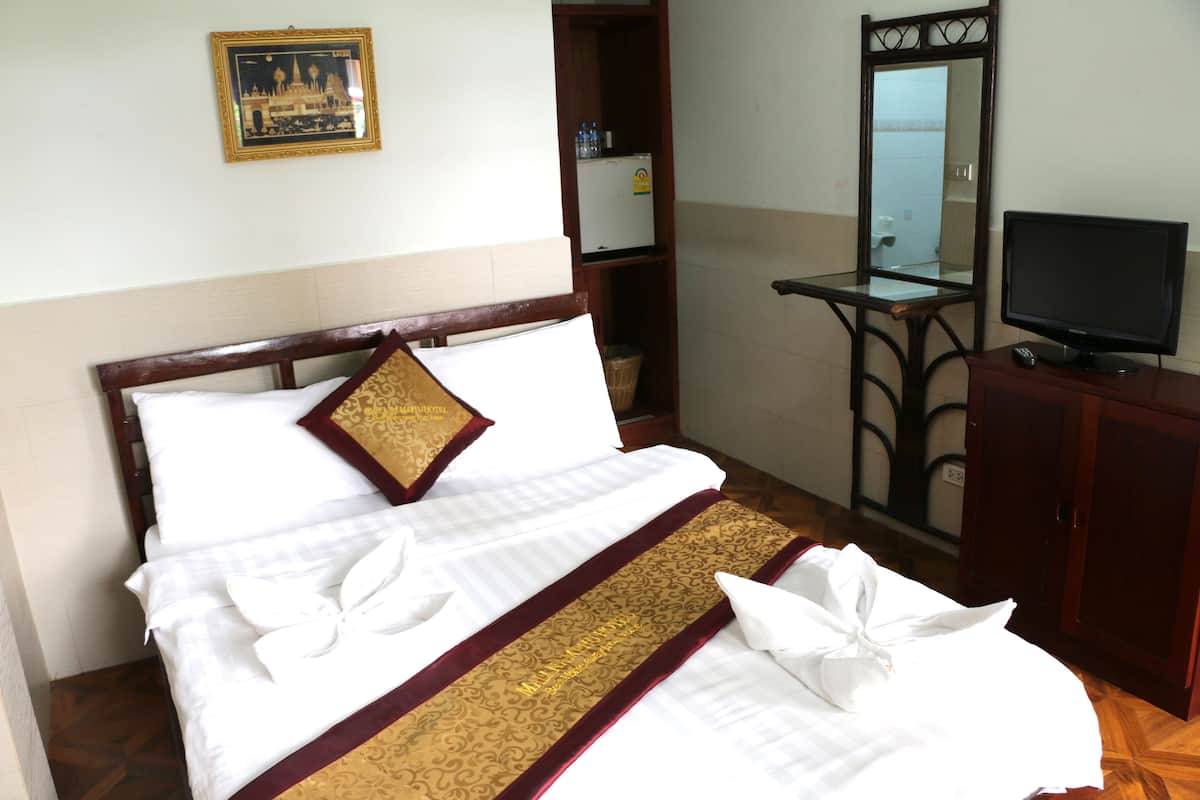 Una cama bien hecha con sábanas blancas y un borde decorativo dorado, un televisor sobre un mueble de madera y un pequeño armario.