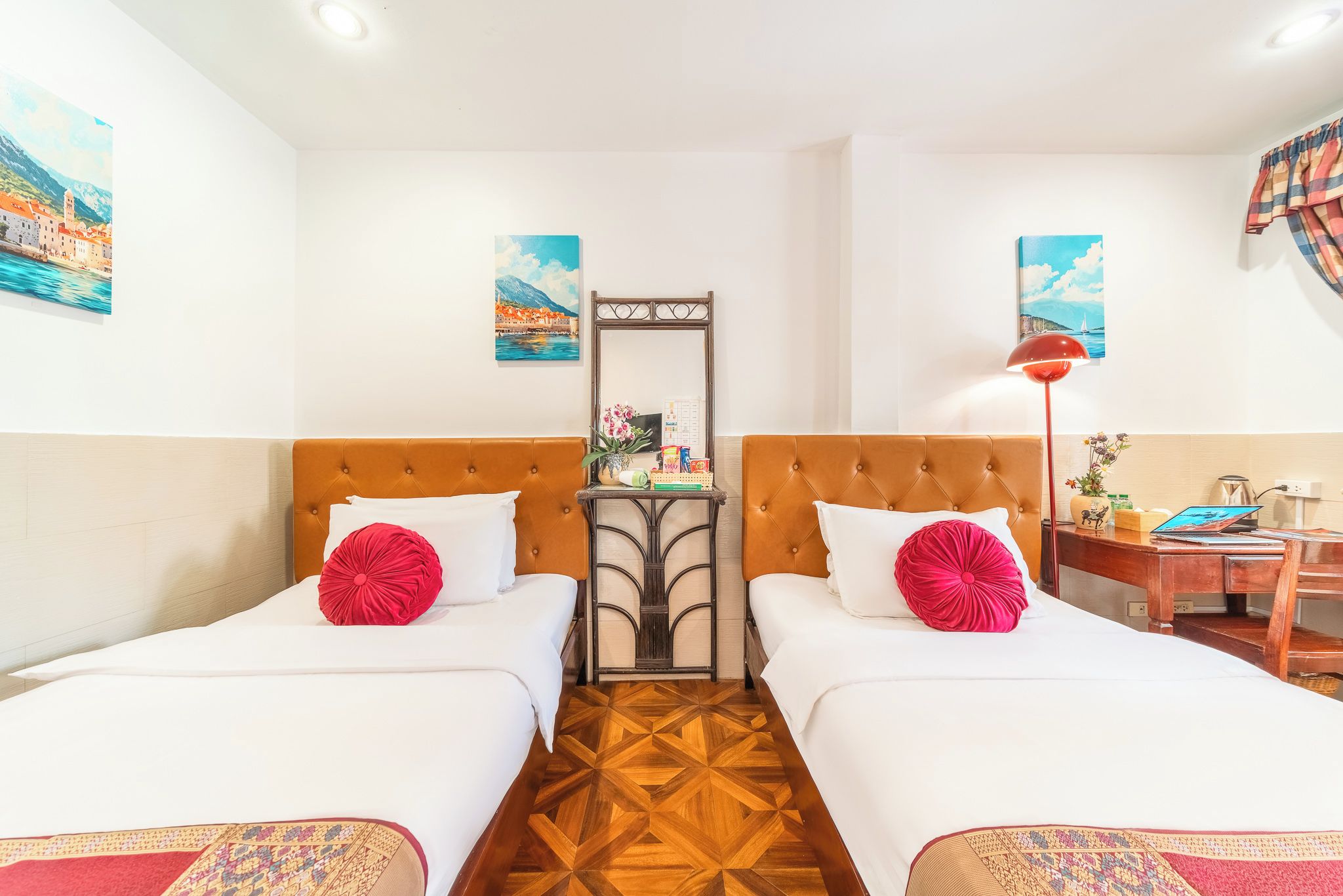 A hotel room with two beds, a small table, a mirror, and artwork on the walls.