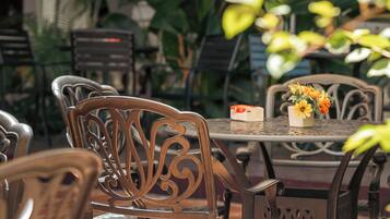 An outdoor patio area with metal chairs and tables, surrounded by potted plants.