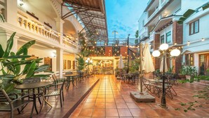 Un área de café al aire libre con mesas y sillas, un espacio de estar central y una escalera que lleva a un nivel superior.