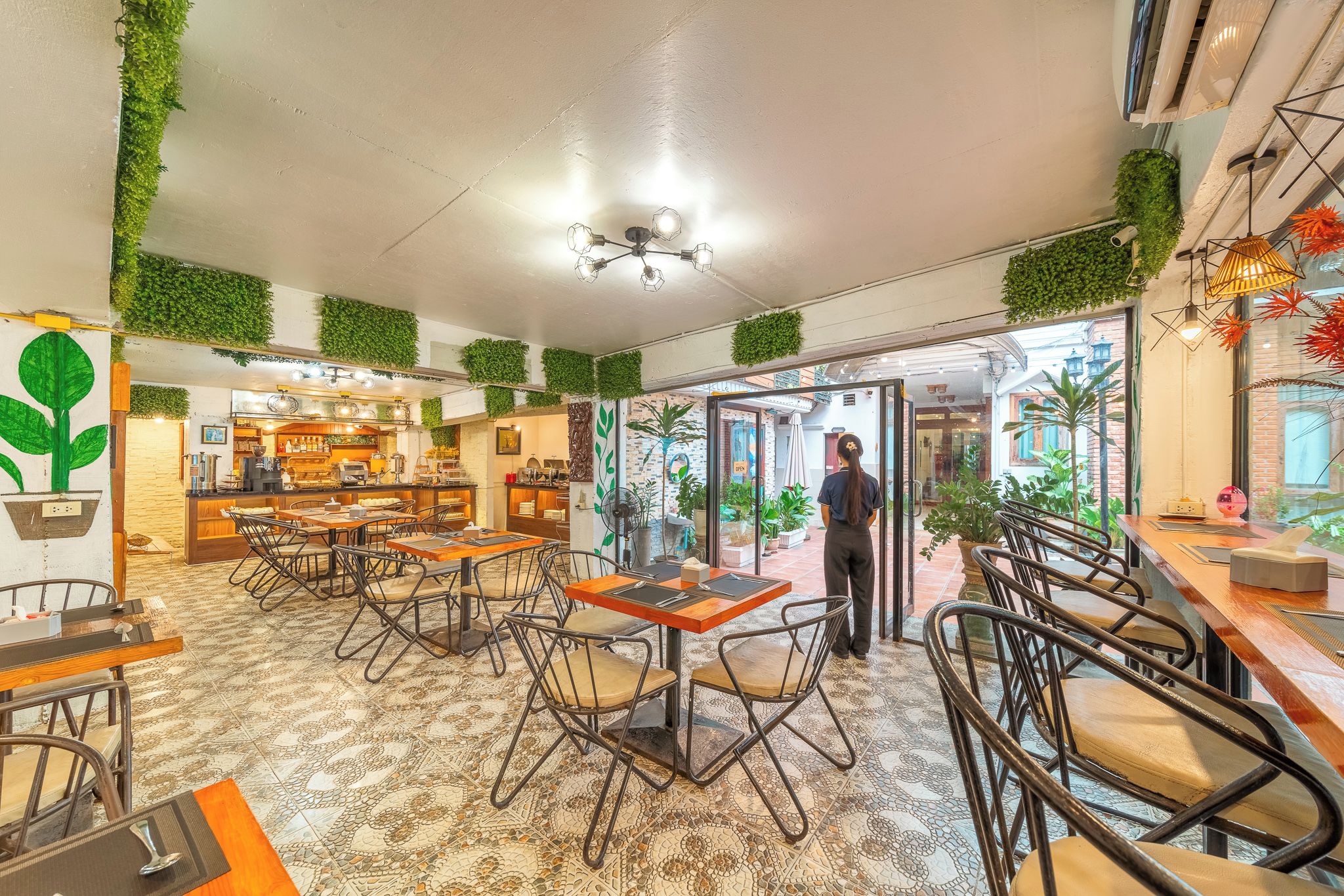 A restaurant interior with tables, chairs, a bar area, and green wall decorations.
