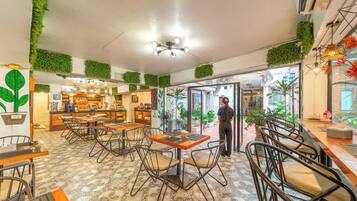 A restaurant interior with tables, chairs, a bar area, and green wall decorations.