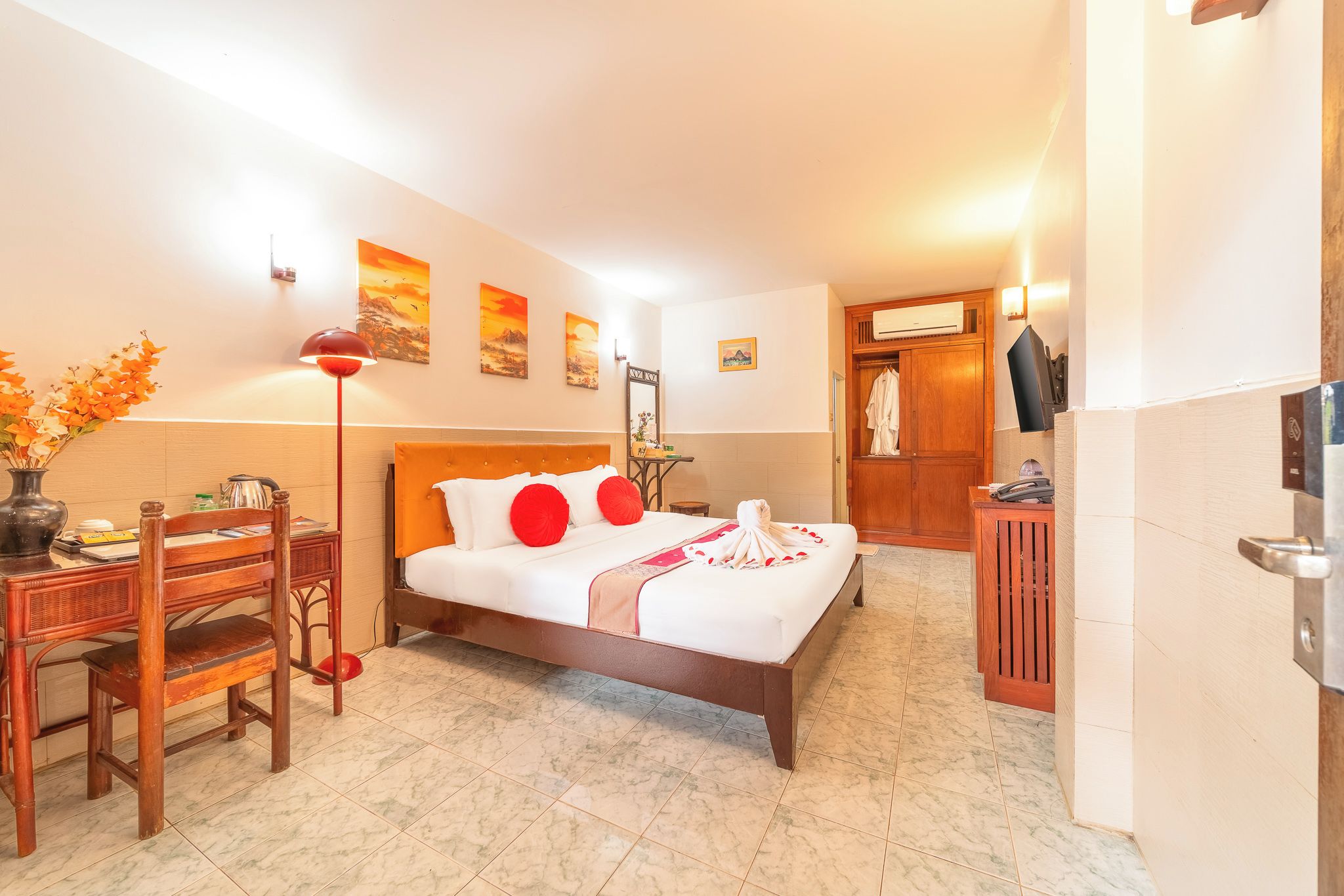 A hotel room with a bed, a desk, a chair, a lamp, and artwork on the walls.