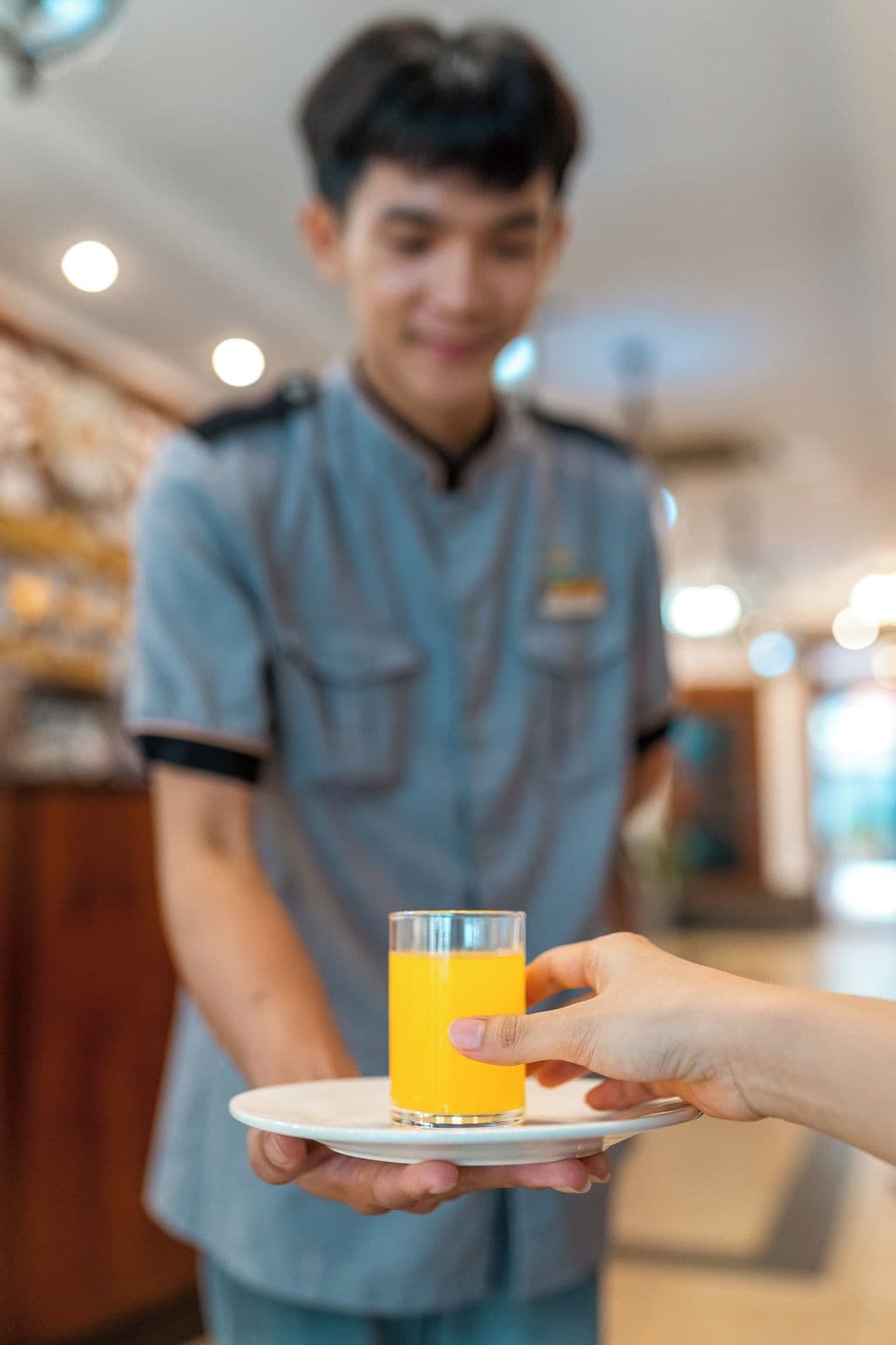 A person in a uniform holding a glass of orange juice on a tray.