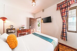 A hotel room with a bed, a desk, a television, and a window with curtains.