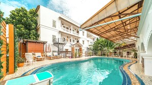 Una piscina con borde de azulejos, sillas de descanso y una zona de estar cubierta.