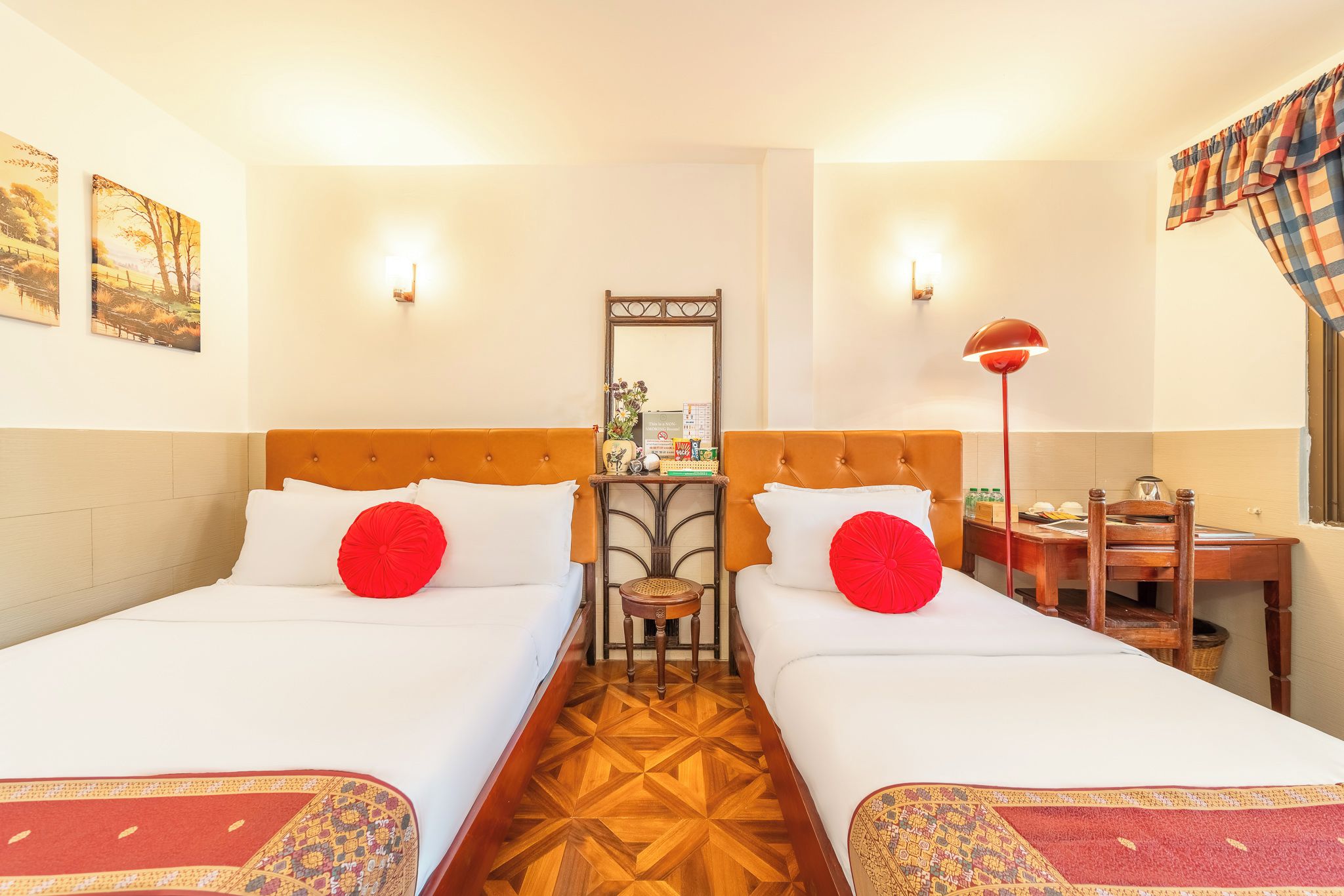 A hotel room with two beds, a wooden floor, a small table with a lamp, and a chair.