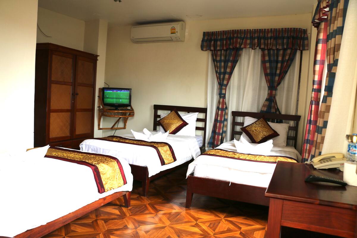 Habitación de hotel con dos camas, televisión, aire acondicionado y teléfono sobre un escritorio.
