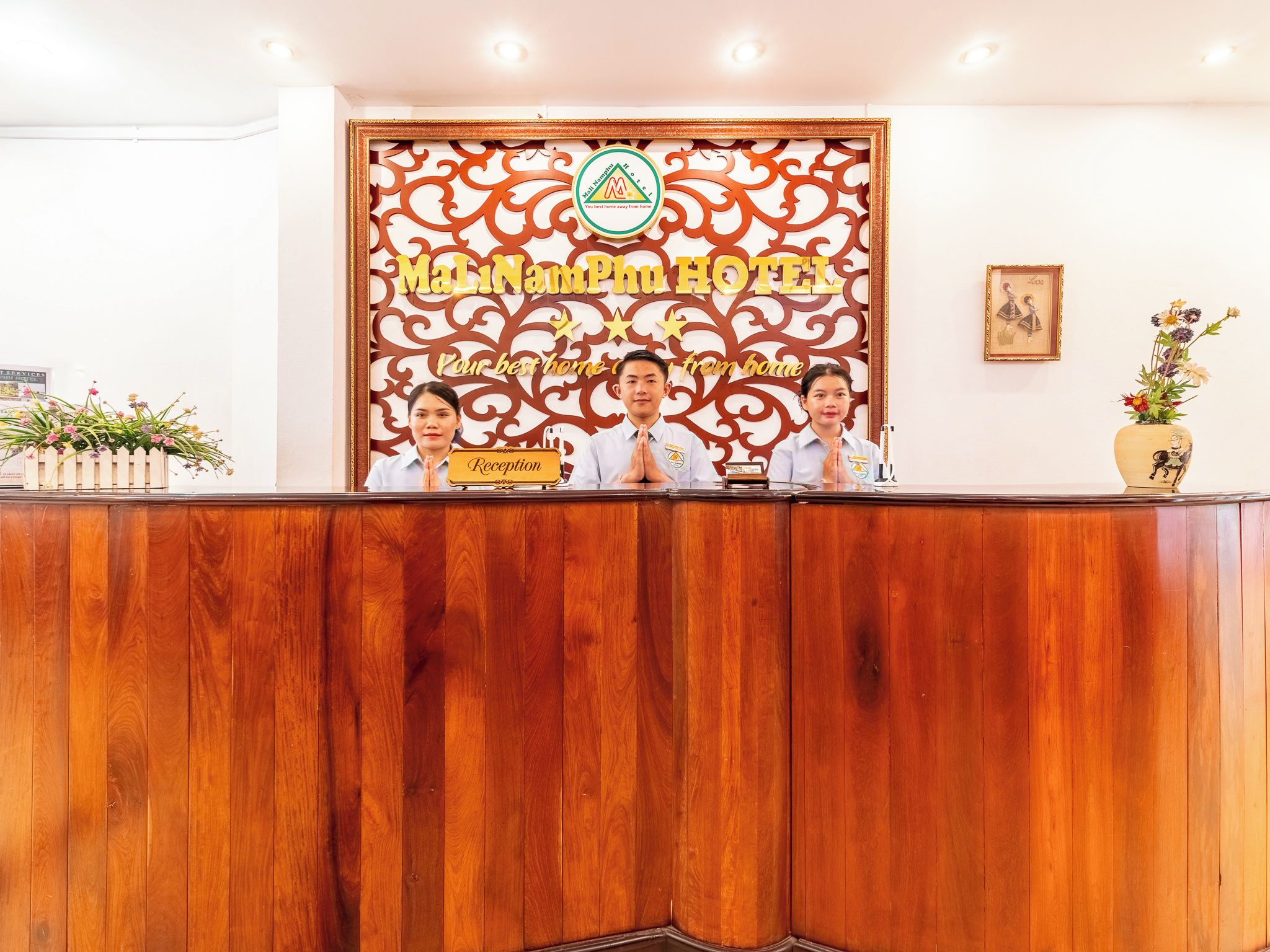 Bancada de recepção com acabamento em madeira, parede decorativa com o nome do hotel e placa de recepção.