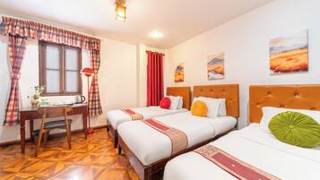 A hotel room with two beds, a desk, and a chair. There are paintings on the wall and a window with curtains.