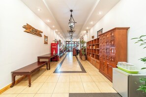 Un pasillo de hotel con un banco de madera, un refrigerador de Coca-Cola, un armario de madera con varios cajones y una planta en maceta.
