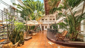 Un amplio patio interior con suelo de baldosas, rodeado de exuberante vegetación tropical y amueblado con asientos exteriores.
