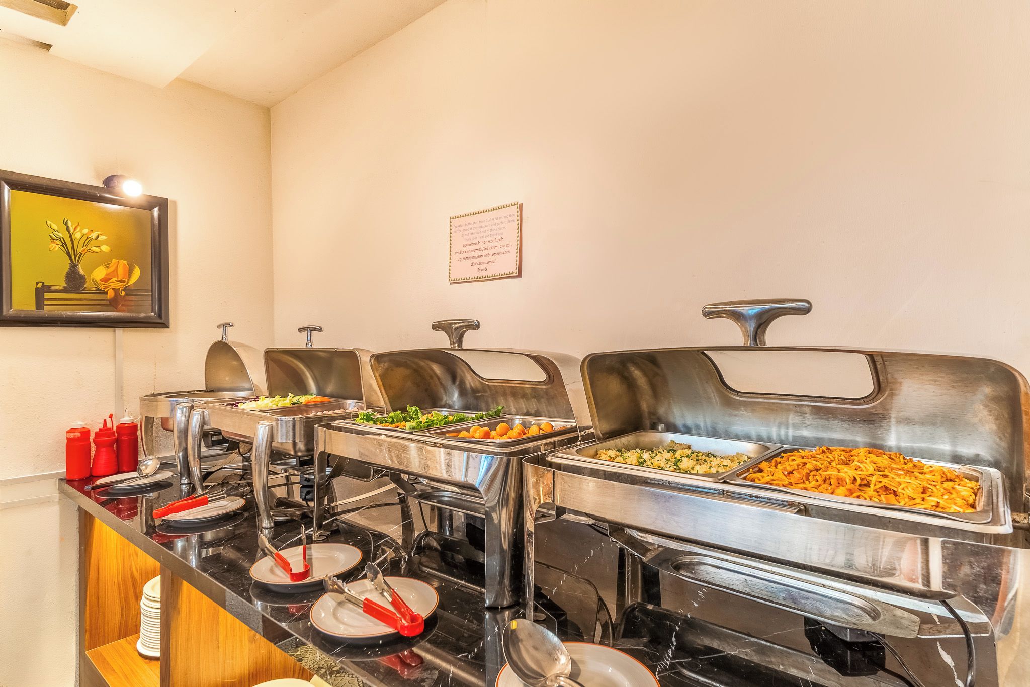 A buffet setup with various food items, serving utensils, and condiments.
