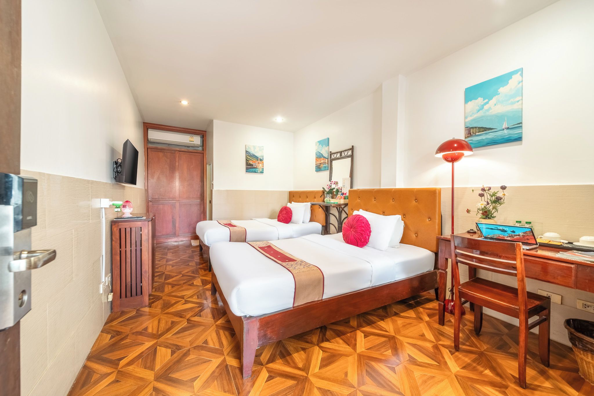 A hotel room with two beds, a desk, a chair, a TV, and a painting on the wall.