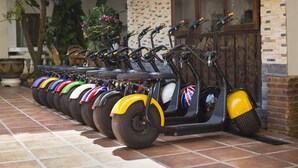 Una fila de scooters eléctricos estacionados frente a un edificio con piso de baldosas y pared de ladrillo.