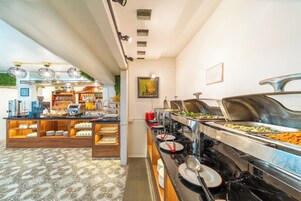 A buffet area with various food stations, a coffee machine, and a seating area with a patterned floor.