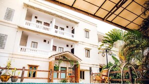 Un edificio de dos pisos con piscina, mobiliario exterior y una zona cubierta con plantas.
