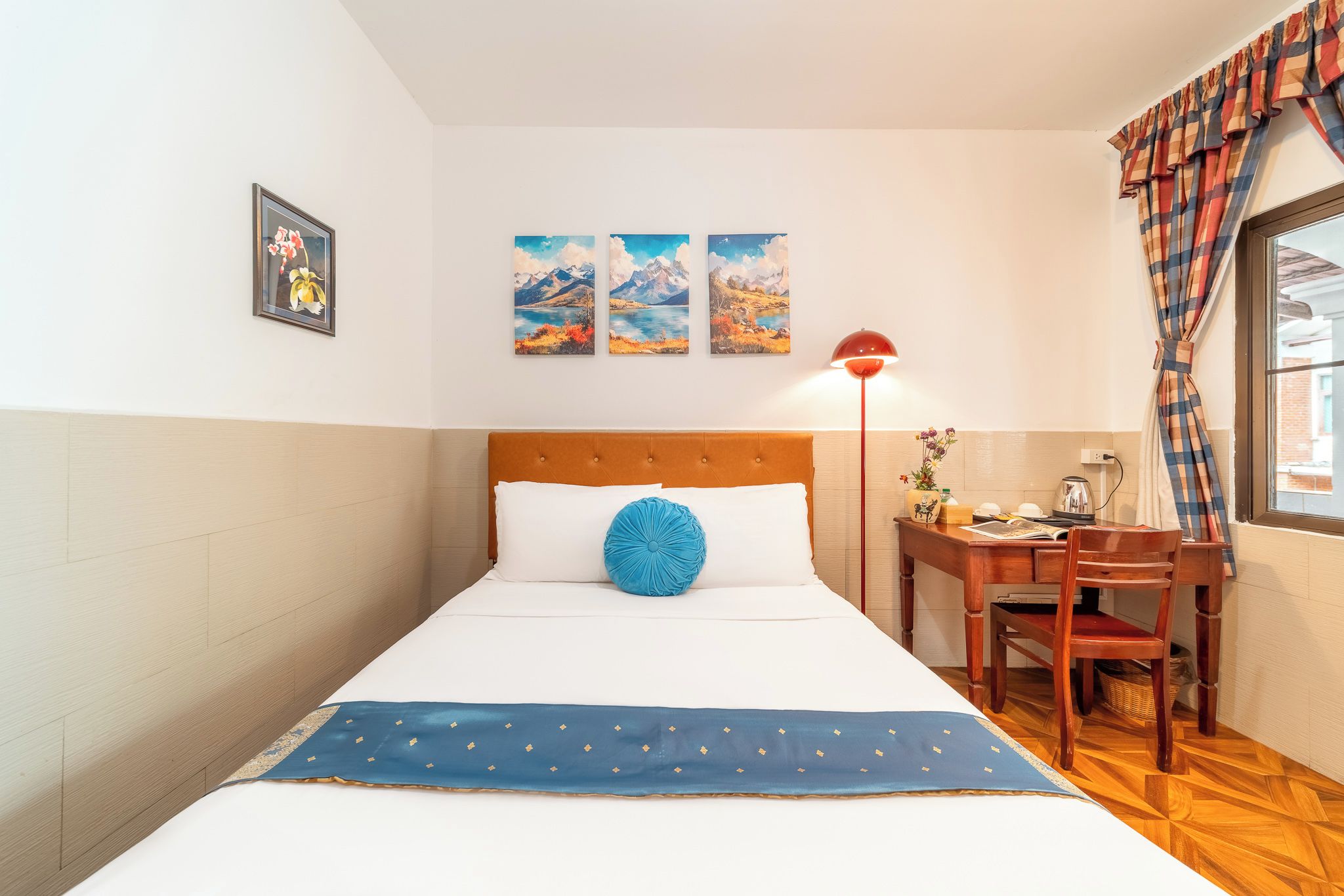 Een keurig opgemaakte hotelkamer met een bed, een bureau en een stoel. Daarboven hangen drie schilderijen aan de muur.