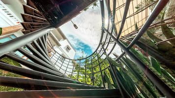 Escadaria em espiral com corrimãos de metal e vista para edifícios e vegetação ao fundo.