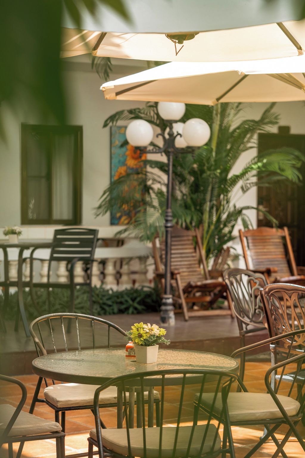 An outdoor seating area with round tables and chairs, a large umbrella, and a decorative lamp post.