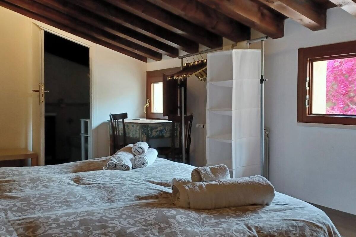 Un dormitorio con una cama, un ventanal con vista a flores rosadas y un techo de madera.
