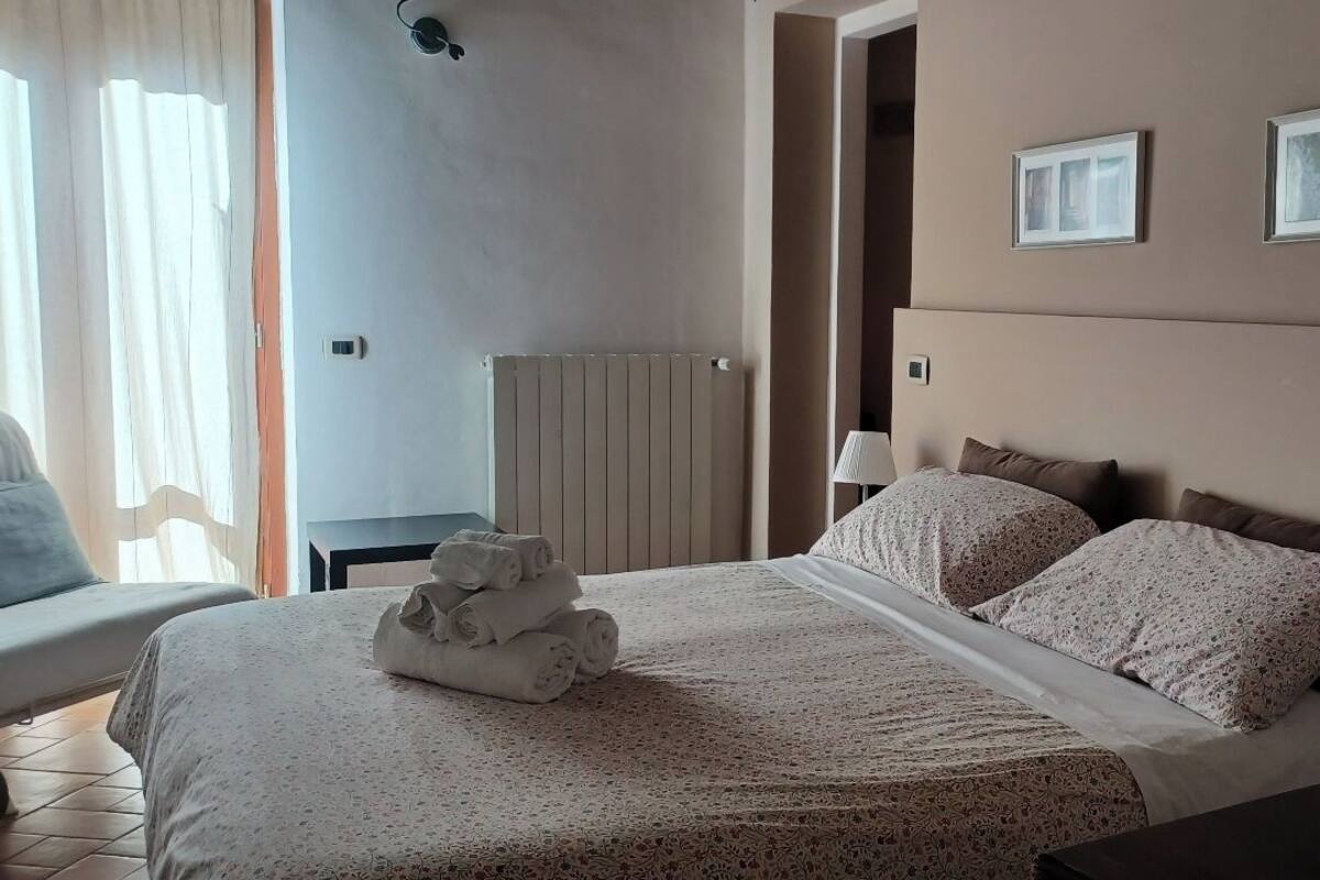 Habitación de hotel con una cama grande, una silla, un radiador y dos cuadros en la pared.