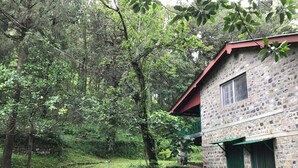 A stone building with a red roof, surrounded by lush greenery and trees. - Fredy's Bungalow (Nainital)
