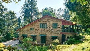 A stone building with a red roof, green shutters, and a porch. - Fredy's Bungalow (Nainital)