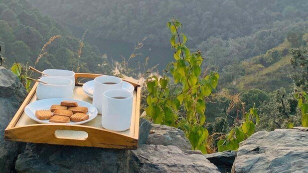 A wooden tray with cups and cookies on a rocky surface with a view of a valley and mountains in the background. - Fredy's Bungalow (Nainital)