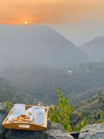 A wooden tray with cups and cookies on a rocky surface with a view of a valley and mountains in the background.