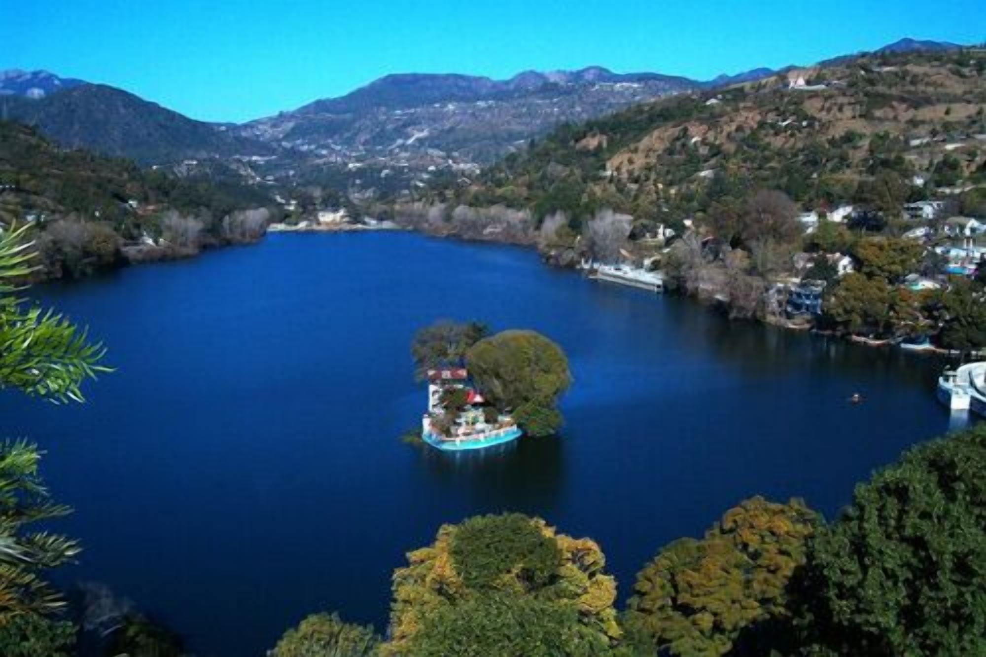 A lake surrounded by hills with a small island featuring a building and a boat.
