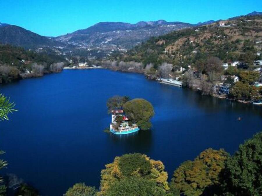 A lake surrounded by hills with a small island featuring a building and a boat.