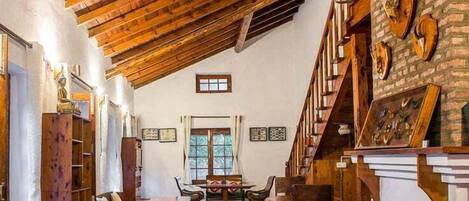 A rustic interior with exposed wooden beams, a brick wall with mounted animal heads, and a wooden staircase.