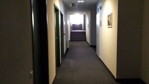 Un couloir étroit, recouvert de moquette, avec des portes de chaque côté, qui mène à un escalier au bout.