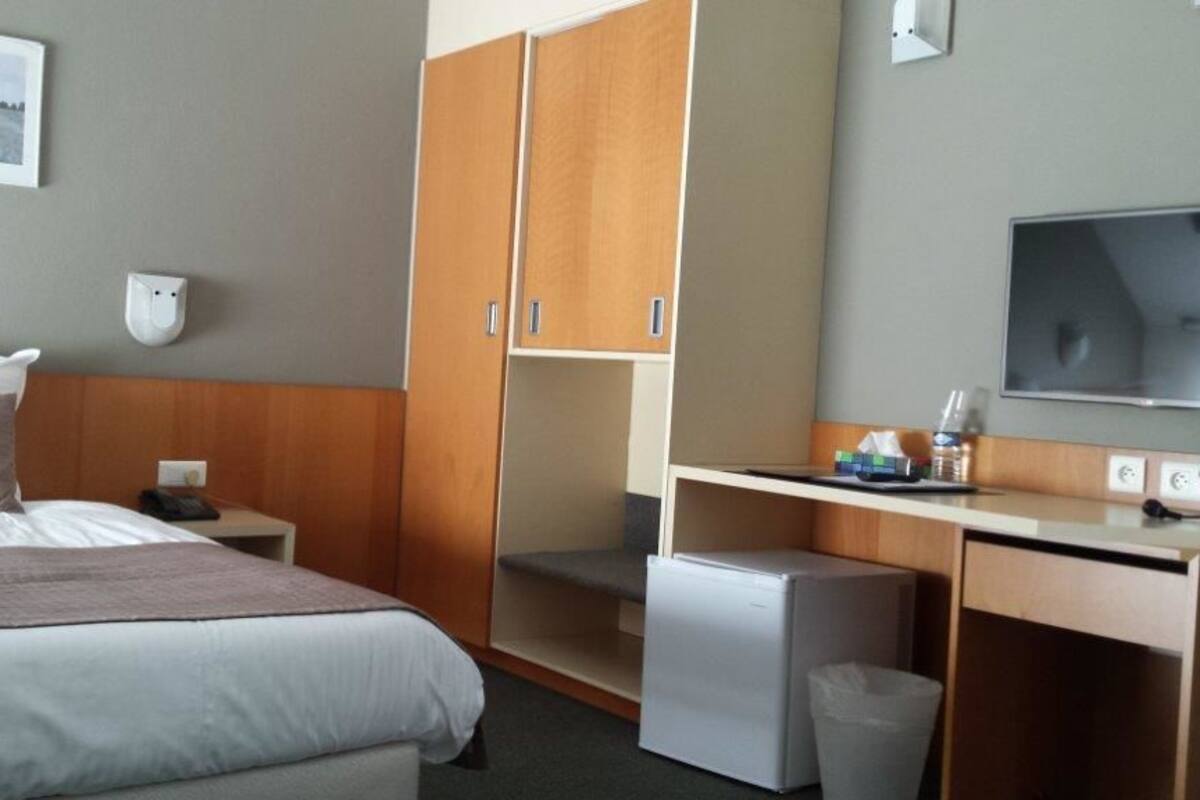 A hotel room with a bed, a desk with a computer, a television, and a small refrigerator.
