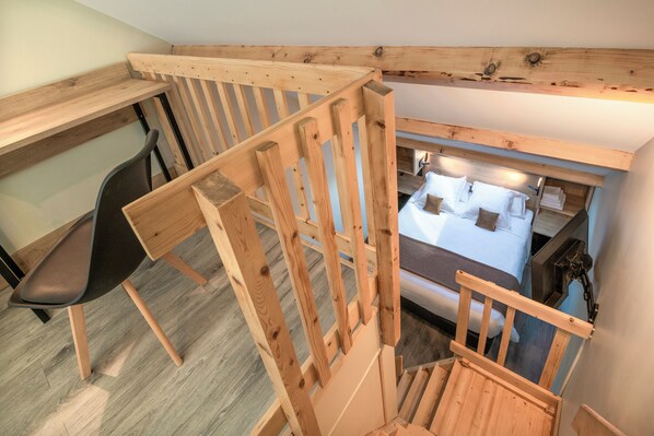 Una escalera de madera que lleva a un dormitorio con una cama, una silla y un escritorio.