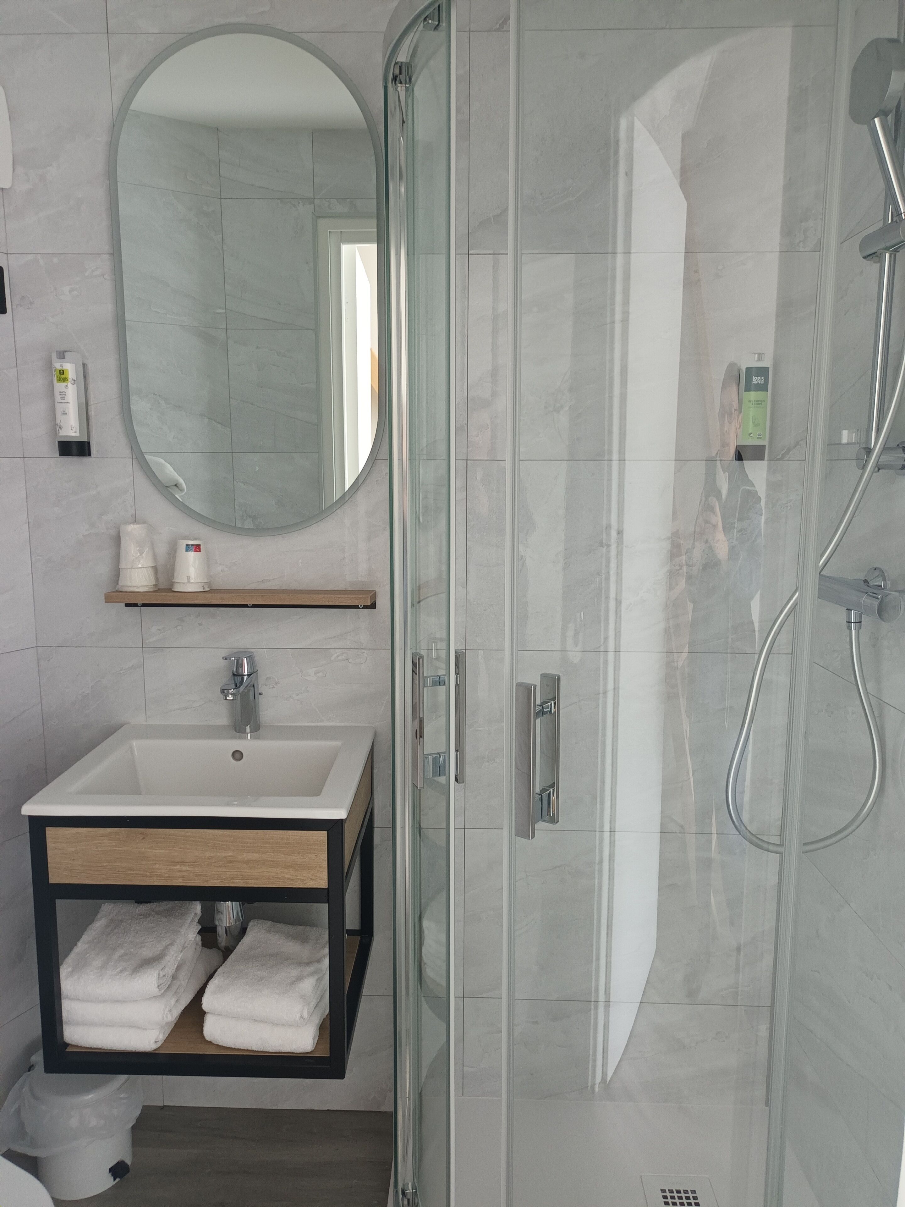 A modern bathroom with a glass-enclosed shower, a sink with a wooden vanity, and a mirror.