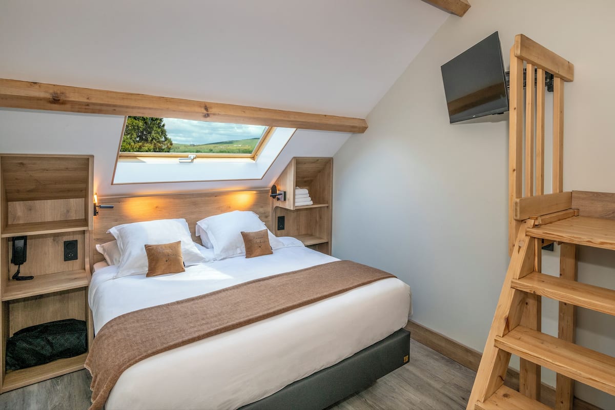 A bedroom with a skylight, a bed with pillows, a bedside table, and a TV mounted on the wall.
