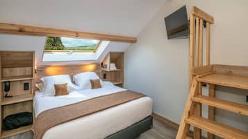 Un dormitorio con tragaluz, cama con almohadas, mesita de noche y televisor montado en la pared.